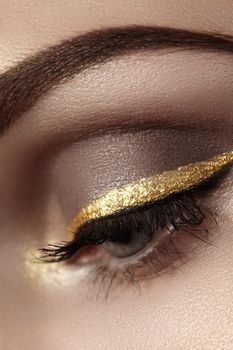 Beautiful macro shot of female eye with ceremonial makeup. Perfect shape of eyebrows, eyeliner and pretty gold line on eyelid. Cosmetics and make-up. Closeup macro shot of fashion sparcle visage