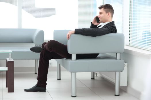 successful businessman sits in the lobby of the office and talking on a smartphone
