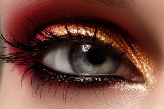 Closeup female eye with beautiful fashion bright make-up. Beautiful shiny gold, pink eyeshadow, wet glitter, black eyeliner