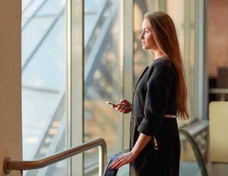 young business woman with mobile phone standing near office window. business concept