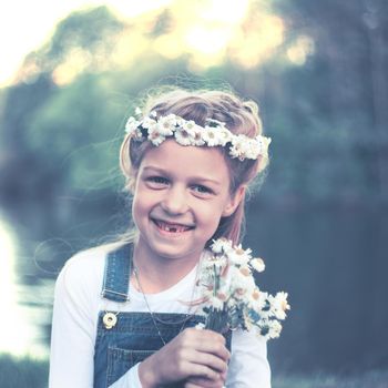 little girl in a wreath of daisies and a bouquet of flowers in the Park on a Sunny day