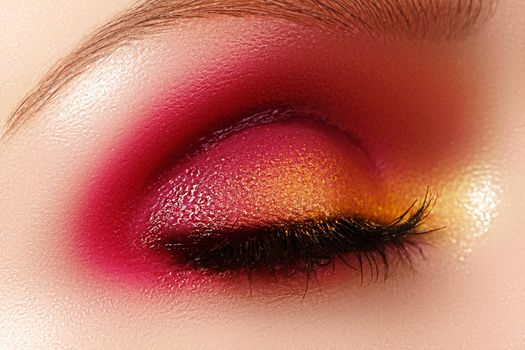Closeup female eye with beautiful fashion bright make-up. Beautiful shiny gold, pink eyeshadow, wet glitter, black eyeliner