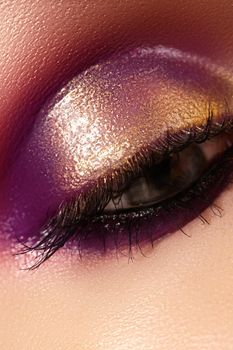 Closeup female eye with beautiful fashion bright make-up. Beautiful shiny gold, pink eyeshadow, wet glitter, black eyeliner