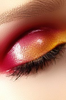 Closeup female eye with beautiful fashion bright make-up. Beautiful shiny gold, pink eyeshadow, wet glitter, black eyeliner