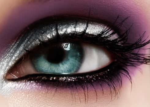 Closeup female eye with beautiful fashion bright make-up. Beautiful shiny silver, purple eyeshadow, wet glitter, black eyeliner