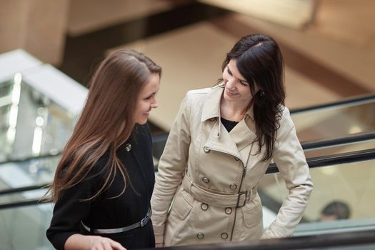 two smiling business women standing on an escalator in a business center. business concept