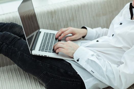 young man looking at laptop screen while lying on sofa .photo with copy space