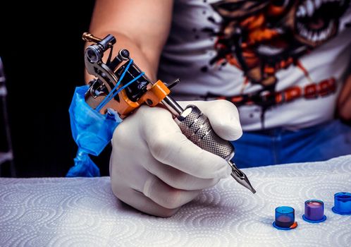 Hand of a tattoo artist, holding a tattoo machine.