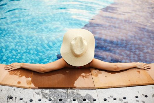 Relaxing on Beach Resort. Beautiful Back Side of Sexy Woman in big Hat Enjoying Vacation from Swimming Pool. Luxury Summer Traveling and Tourism Concept