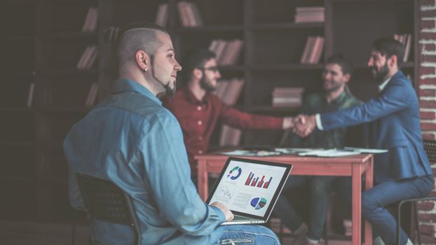 financial administrator works with financial graphs on the background of business partners handshaking in a modern office