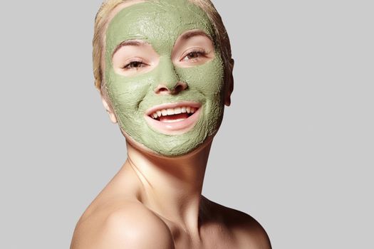 Beautiful Woman Applying Green Facial Mask. Beauty Treatments. Close-up Portrait of Spa Girl Apply Clay Facial mask on grey background