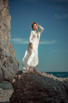 Middle aged woman looks good with blond hair, boho style in white long dress on the beach decorations on her neck and arms