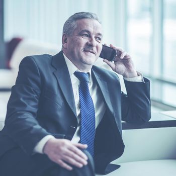 experienced businessman talking on smartphone sitting on couch in the office.