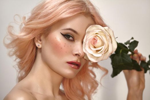Soft-Girl Style with Trend Pink Flying Hair, Fashion Make-up. Woman Face with Fake Freckles and Rose Flower. Blonde Female Model with perfect Fresh Clean Skin, Blush Rouge. Wedding Bride Makeup