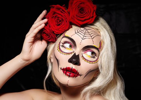 Beautiful Halloween Make-Up Style. Blond Model Wear Sugar Skull Makeup with Red Roses, pale Skin Tones and Waves Hair. Santa Muerte concept