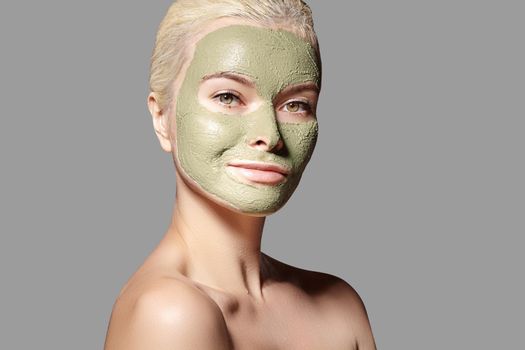 Beautiful Woman Applying Green Facial Mask. Beauty Treatments. Close-up Portrait of Spa Girl Apply Clay Facial mask on grey background.