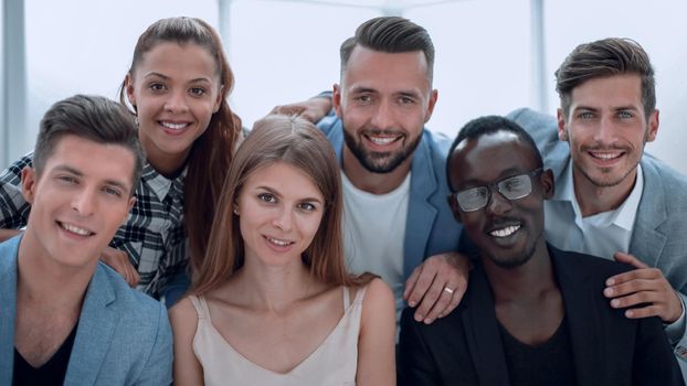 Portrait of a smiling group of diverse corporate colleagues standing in a row together at a table in a bright modern office