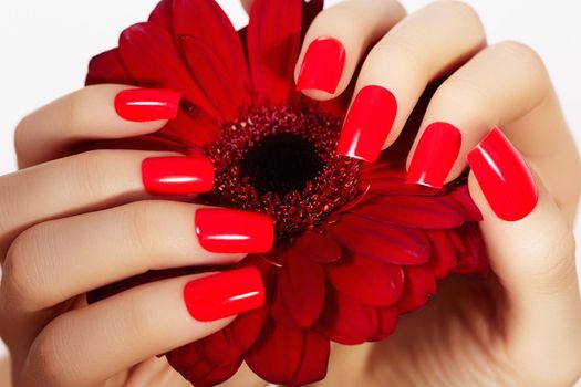 Beauty hands with red fashion manicure and bright flower. Beautiful manicured red polish on nails. Fasionable cosmatics and makeup