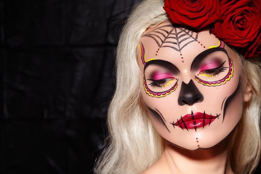 Beautiful Halloween Make-Up Style. Blond Model Wear Sugar Skull Makeup with Red Roses, pale Skin Tones and Waves Hair. Santa Muerte concept