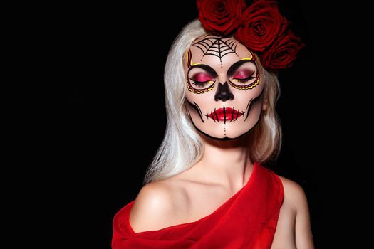 Beautiful Halloween Make-Up Style. Blond Model Wear Sugar Skull Makeup with Red Roses, pale Skin Tones and Waves Hair. Santa Muerte concept