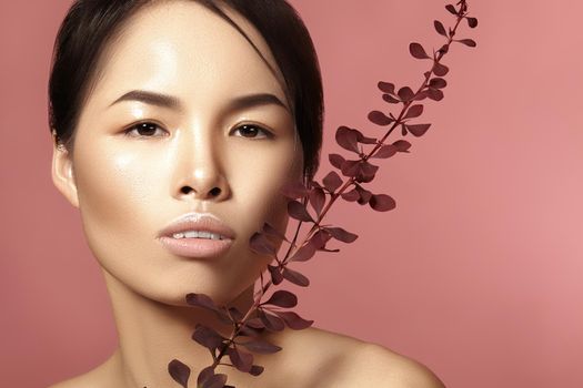 Beautiful asian woman with fresh daily makeup. Vietnamese beauty girl in spa treatment with green leafs near face. Pink background
