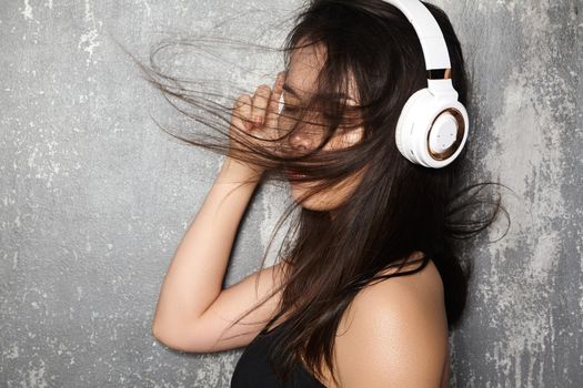 Beautiful sport woman with big white headphones. Model listening the music. Fitness portrait on gray wall. Perfect body shapes