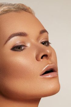 Close-up face of beautiful young woman with smooth tanned skin. Portrait of beauty model with natural bronze make-up. Spa, skincare and wellness