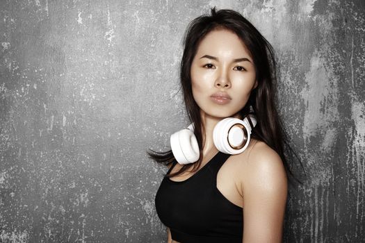 Beautiful sport woman with big white headphones. Model listening the music. Fitness portrait on gray wall. Perfect body shapes