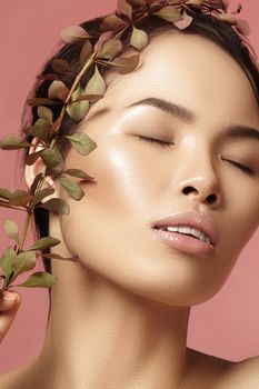 Beautiful asian woman with fresh daily makeup. Vietnamese beauty girl in spa treatment with green leafs near face. Pink background