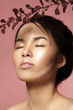 Beautiful asian woman with fresh daily makeup. Vietnamese beauty girl in spa treatment with green leafs near face. Pink background
