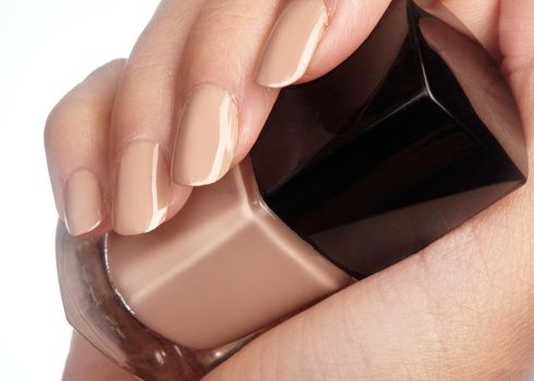 Beautiful female fingers with ideal naturel shiny beige manicure holding nail polish bottle. Care about female hands, healthy soft skin. Spa, cosmetics.