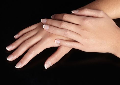 Beautiful female arms with ideal french manicure on black background. Care about female hands, healthy soft skin. Spa and cosmetics. Beauty care. Close-up of beautiful famele fingers with nails polish