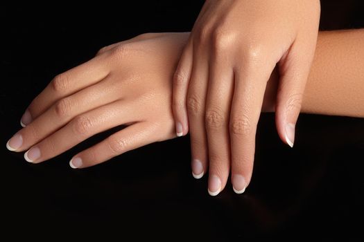 Beautiful female arms with ideal french manicure on black background. Care about female hands, healthy soft skin. Spa and cosmetics. Beauty care. Close-up of beautiful famele fingers with nails polish