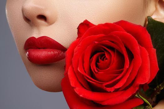 Close-up beautiful female lips with bright lipgloss makeup. Perfect clean skin, light fresh lip make-up. Beautiful spa portrait with tender pink rose flower. Spa and cosmetics
