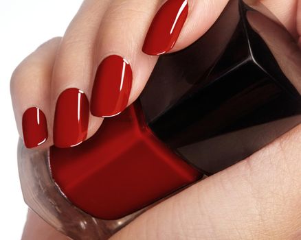 Beautiful female fingers with ideal shiny red manicure holding nail polish bottle. Care about female hands. Bright gel nails