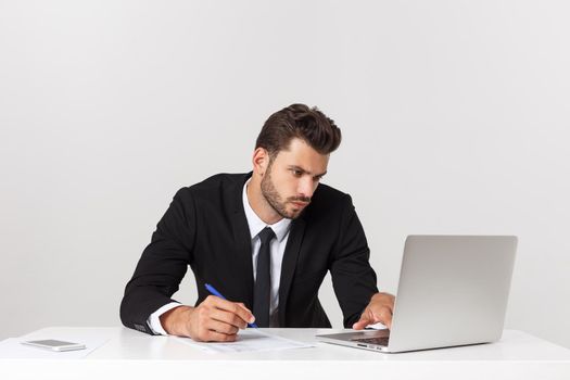 Serious handsome businessman working in the office,front view with laptop, isolated on white