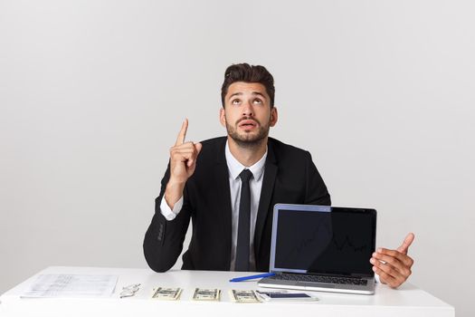 Business Concept: Portrait of handsome businessman dressed in suit sitting in office pointing finger at copy space and laptop isolated over gray background