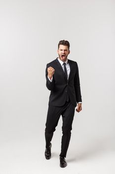 Cheerful young bearded business man show hand up excited with clenched fists. Full length portrait business man isolated over white studio background.