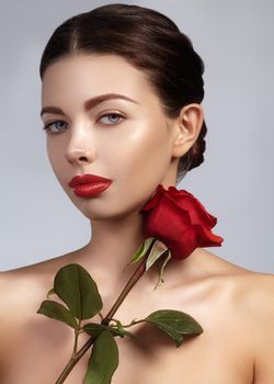Close-up beautiful young woman with bright lipgloss makeup. Perfect clean skin, sexy red lip make-up. Beautiful valentine visage with red rose flower. Romantic and sexy look for Valentines day.