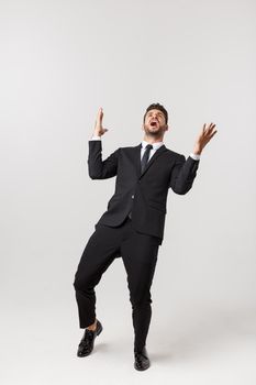 Cheerful young bearded business man show hand up excited with clenched fists. Full length portrait business man isolated over white studio background.