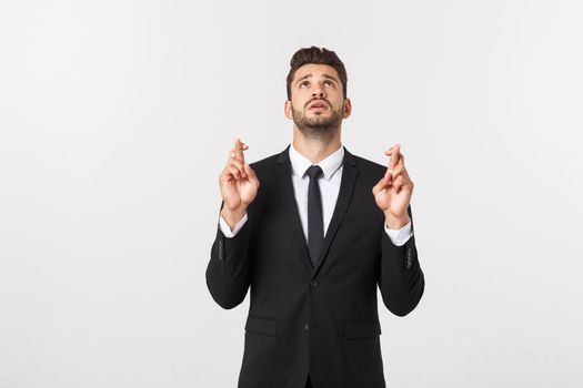 Businessman fingers cross on copy space. Handsome young man in suit looking at camera while standing against white background