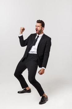 Cheerful young bearded business man show hand up excited with clenched fists. Full length portrait business man isolated over white studio background.