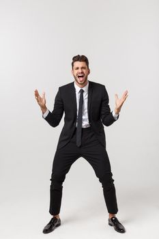 Cheerful young bearded business man show hand up excited with clenched fists. Full length portrait business man isolated over white studio background.