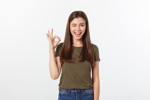 Happy young woman showing ok sign with fingers an winking isolated on a gray background