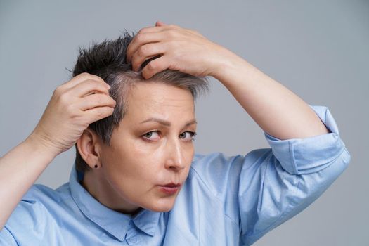 Portrait of mature woman in 50s checking her hair and unhappy to see a results in mirror. Beautiful grey haired woman dealing with dandruff problem checking in mirror.