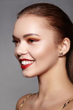 Closeup portrait of smiling Woman Face with Gold glitter Make-up, bright red liner on Eyes. Fashion Celebrate Makeup, Glowy Skin. Shiny Simmer and metalic eye shadows