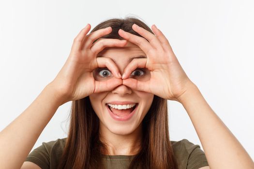 Close up portrait of cheerful, cute, stylish,attractive, trendy girl making binoculars with fingers, isolated on grey background, having good mood.