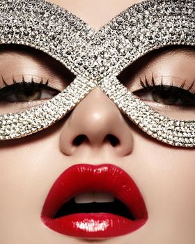 Beautiful Model with Fashion luxe Lips Make-up wearing bright brilliant mask. Masquerade style woman. Holiday celebration look