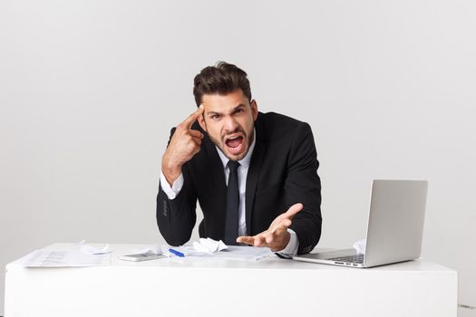 Angry and desperate caucasian entrepreneur businessman shouting at computer feeling tired and overworked at desk in People, Stress, Technology and Overtime concept isolated in white background.