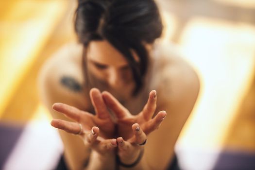 Close up of a young woman is doing yoga Lotus mudra - symbol of purity, this mudra opens the heart. She is meditating on floor mat in morning sunshine at home.